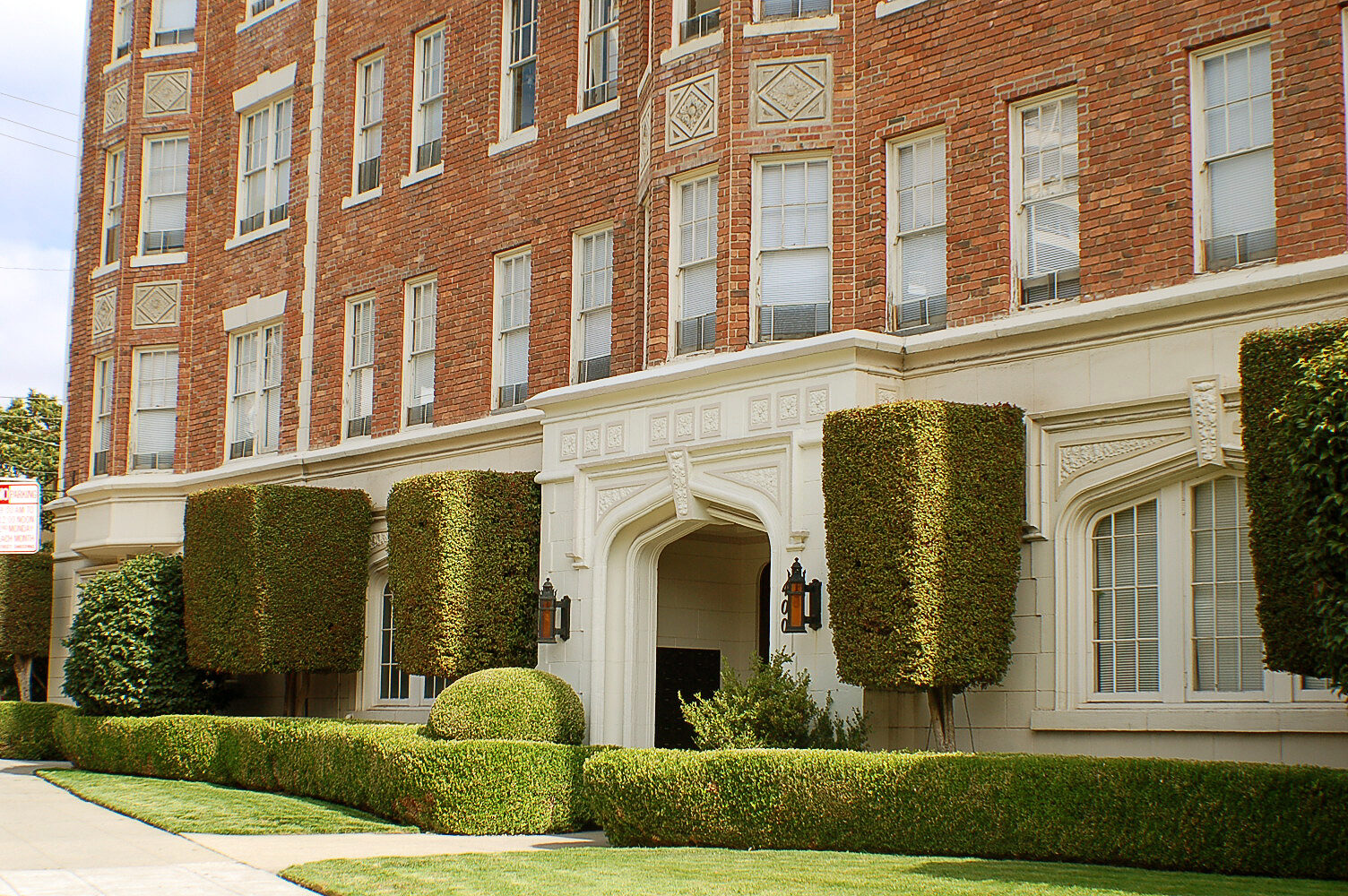 Red brick Tudor Revival apartment building with a carved stone arched entry and clipped hedges